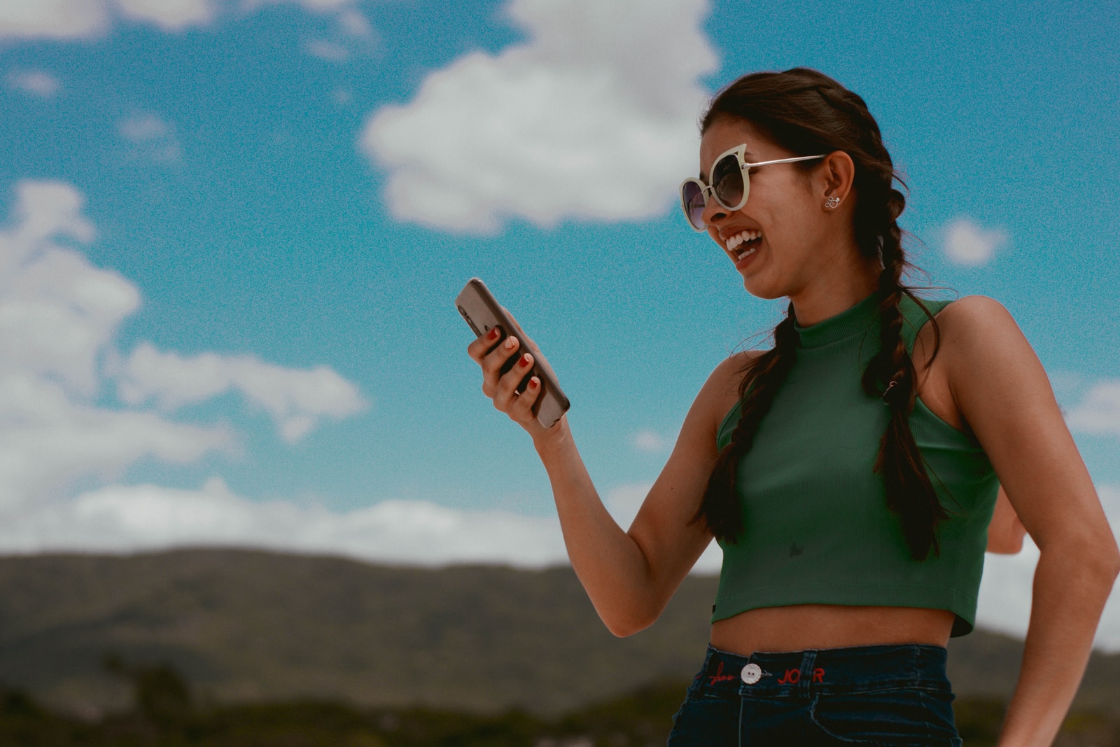 woman in green tank top holding smartphone during daytime